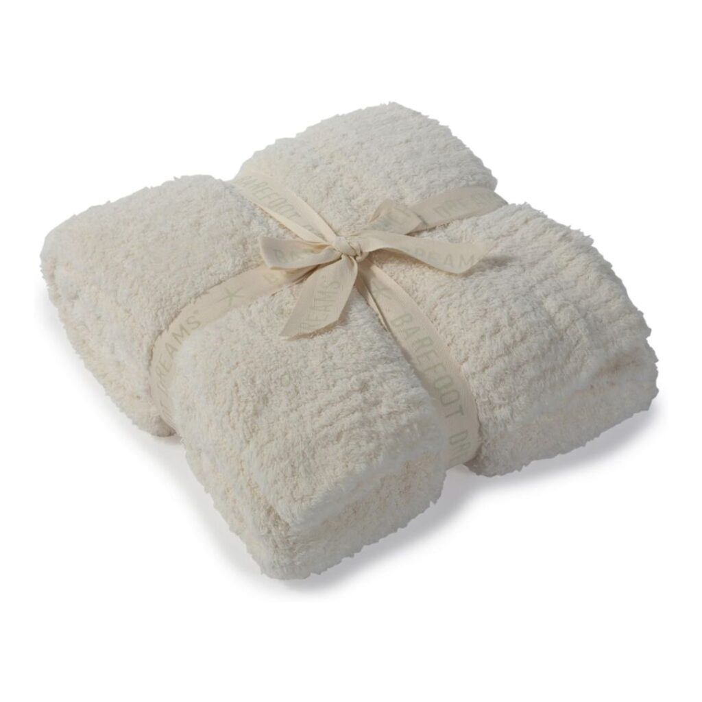 A neatly folded, fluffy white blanket tied with a beige ribbon is displayed. The blanket has a soft, textured appearance, perfect for cozying up in lakehouse decor. The ribbon features text and decorative elements, adding an elegant touch.