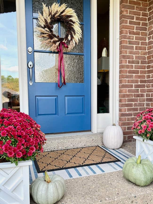 Pair green heirloom pumpkins with red mums in white planter boxes on the front porch.