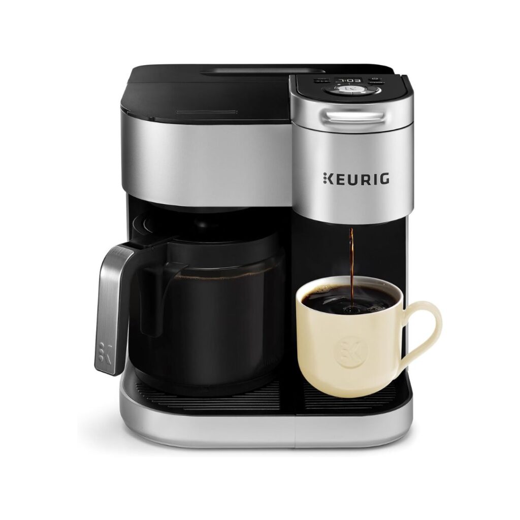 A Keurig coffee maker with a black and silver design fits seamlessly into lakehouse decor. It is brewing coffee into a cream-colored mug placed on the machine's drip tray, while a black carafe with a handle sits beside the mug, ready to hold more coffee.