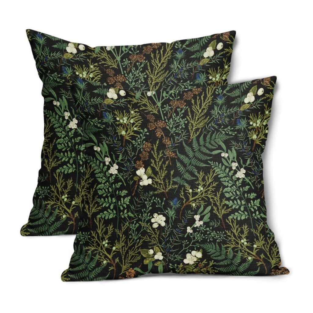 Two decorative pillows featuring a lush, botanical pattern on a dark background perfectly capture the essence of lakehouse decor. The design showcases various green leaves, ferns, sprigs, and delicate white flowers, creating a natural and serene aesthetic. The pillows are arranged slightly overlapping.