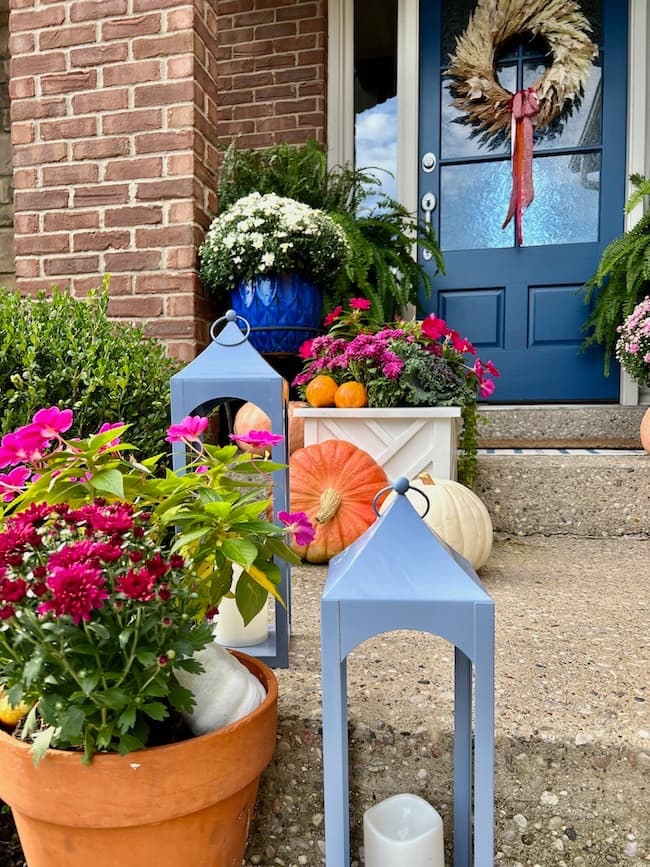 Blue lanterns with purple and red mums, orange and white pumpkins for fall porch
