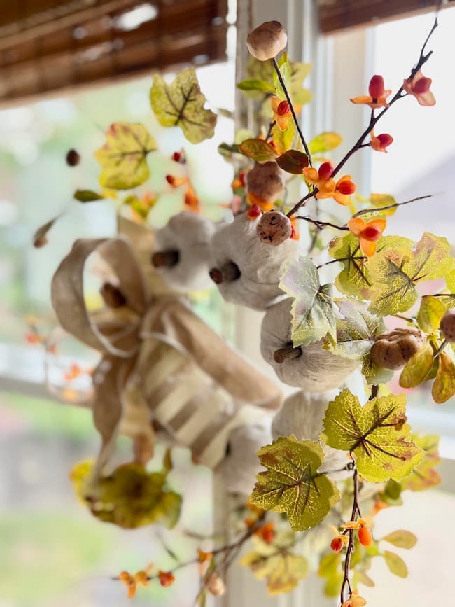 Mini fall wreath with white pumpkins and orange berries in window