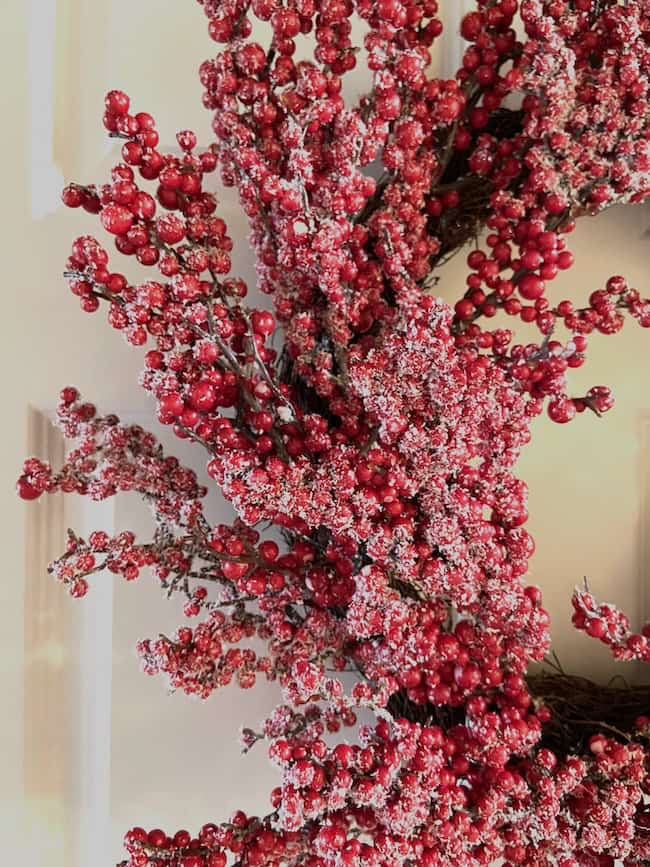 A festive wreath, embodying Christmas theme ideas for decorating, showcases red berries dusted with snow, elegantly hung against a light-colored background.