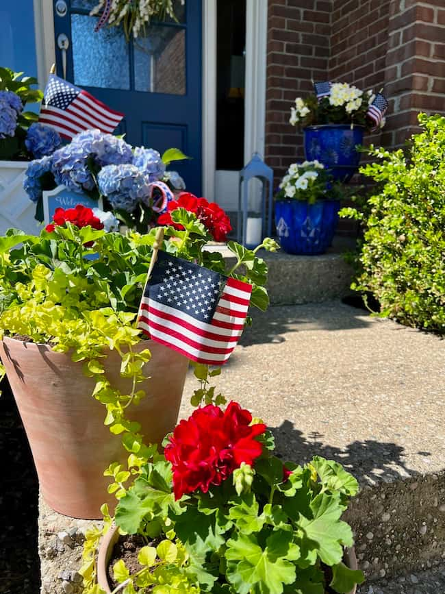 Patriotic flower pots with red geraniums and American flags in terracotta pots.