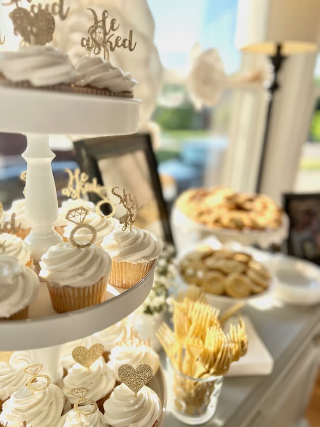 Engagement party dessert table with cupcakes on a three tiered stand and cookies on various pedestals