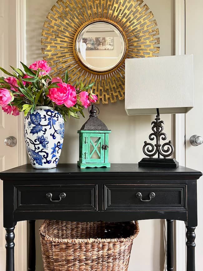 Foyer entryway table decorated with texture -- gold metal mirror, woven basket, painted wood lantern with metal tope, pottery