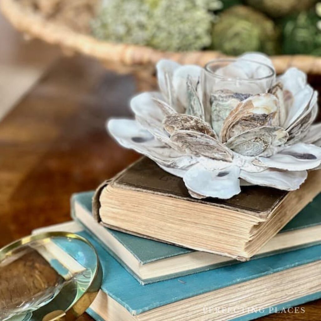 Add texture to a room with textural elements on coffee table -- oyster shell votive holder, stack of vintage books, magnifying glass, moss covered balls in woven basket.