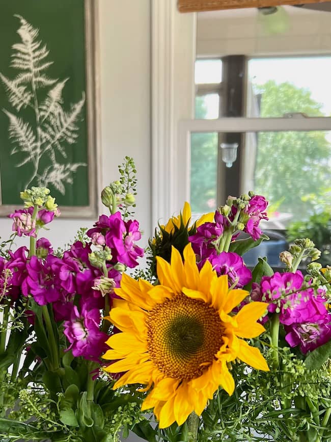 Sunflowers and purple stock arranged with greenery in a bud vase holder on the kitchen table