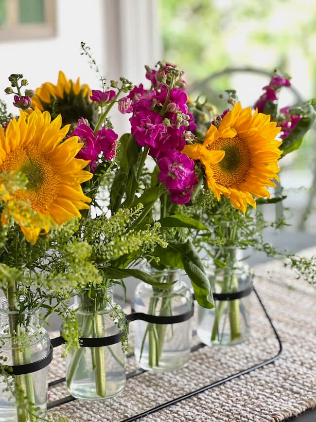 Sunflowers and purple stock arranged with greenery in a bud vase holder on the kitchen table