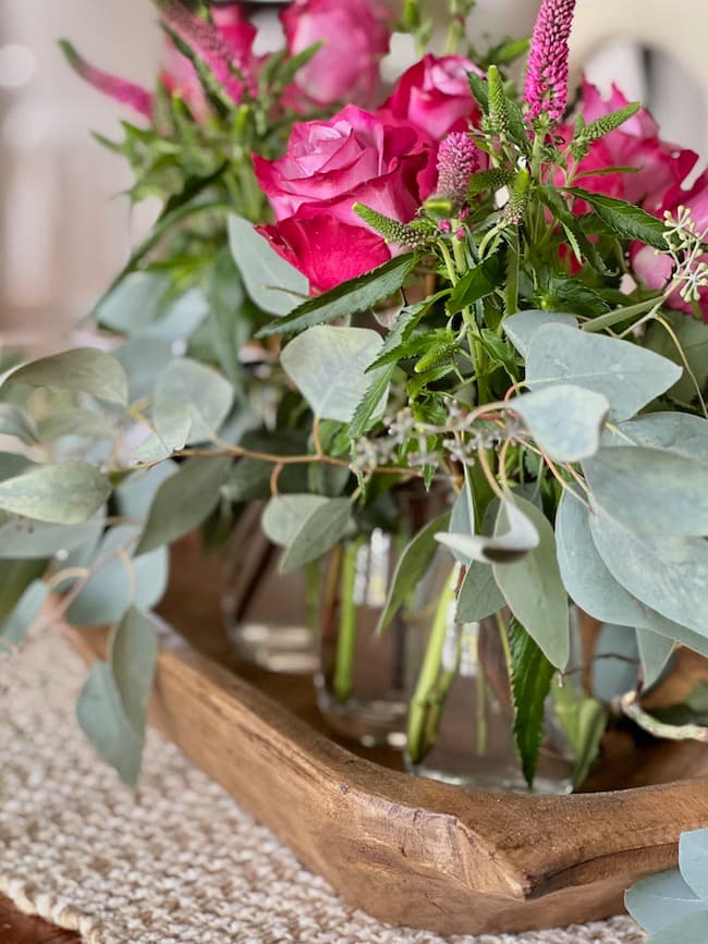Deep pink roses and eucalyptus arranged in bud vase centerpiece in wooden dough bowl