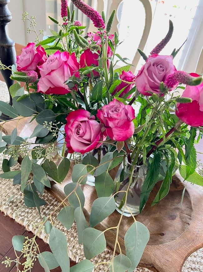 Deep pink roses and eucalyptus arranged in bud vase centerpiece in wooden dough bowl