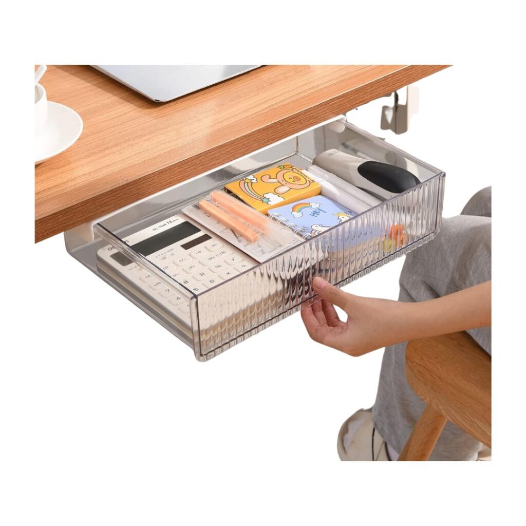 A transparent desk drawer attached beneath a wooden tabletop holds various items including a calculator, colorful pens, notebooks, and other stationery. A person in gray pants and white shoes is partially visible, reaching to organize the drawer with tips for getting organized.