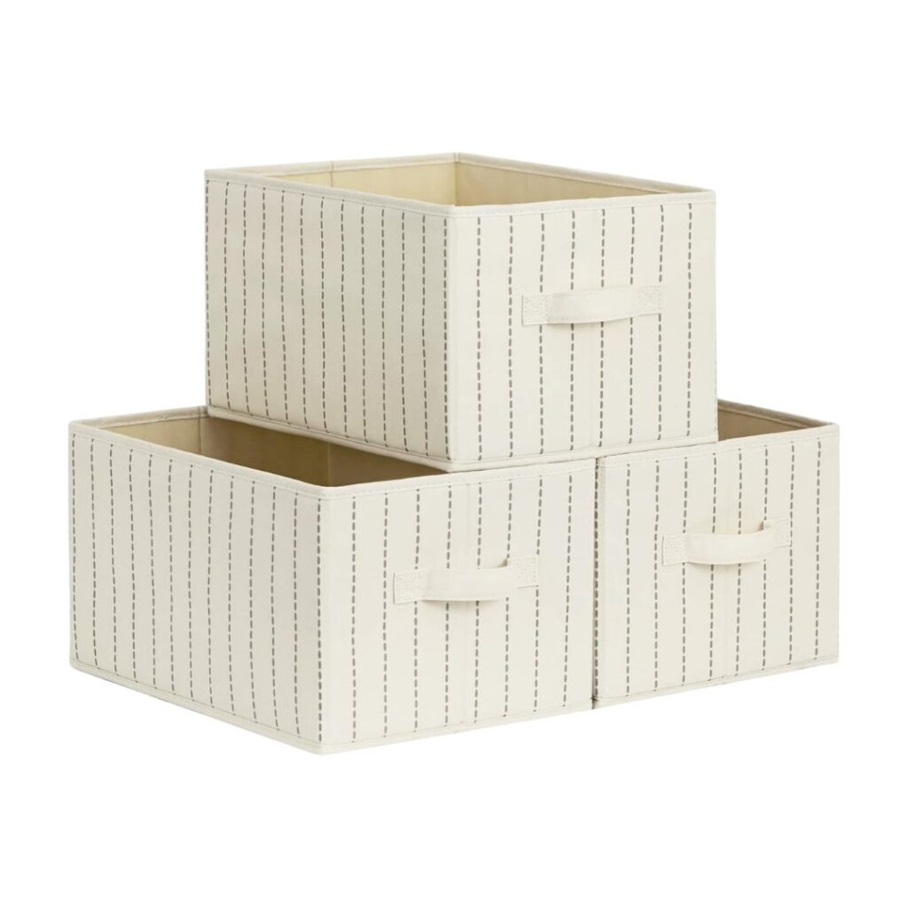 Three beige storage boxes with vertical gray stripes are stacked, offering practical tips for getting organized. One box sits on top of two side-by-side boxes, each featuring a handle on the front for easy access. The background is white.