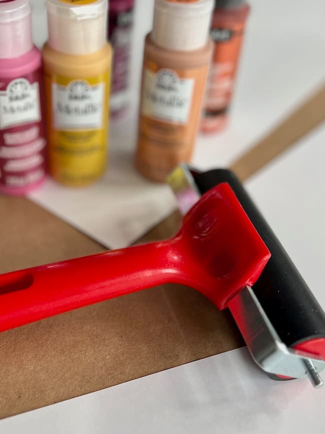 Metallic paint for painting leaves in the garland shades of pink, rust, gold, and terracotta and a rubber brayer for rolling the paint on.