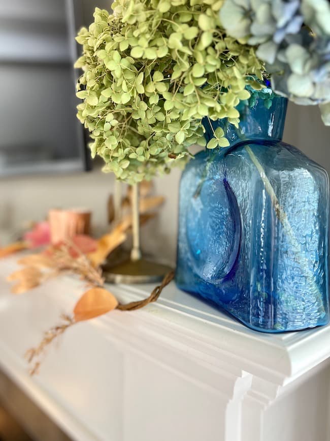 Blue glass vase full of dried hydrangeas on the mantel with the fall leaf garland