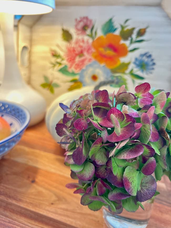 Fall Decor on Kitchen Countertops with a dried hydrangea bloom, vintage tole painted tray, blue and white bowl, red apples on a wooden cutting board.