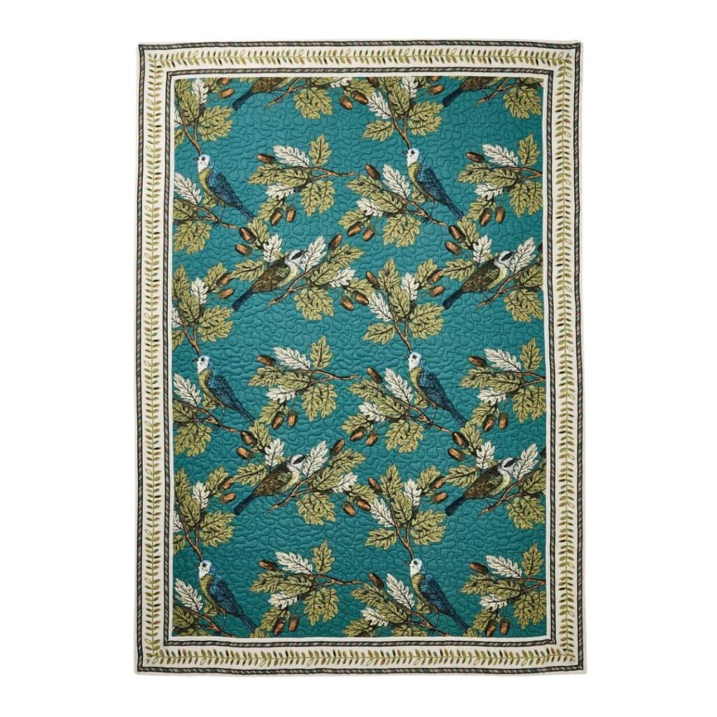 A rectangular quilt with a vibrant design featuring birds perched on leafy branches, perfect for fall kitchen decor on a budget. The teal background and leaf-patterned border enhance its charm, while the intricate stitching adds a touch of elegance.