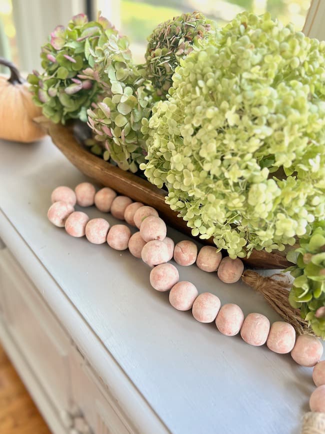 DIY terracotta bead garland with air-dry clay draped on kitchen buffet with dough bowl and dried hydrangeas