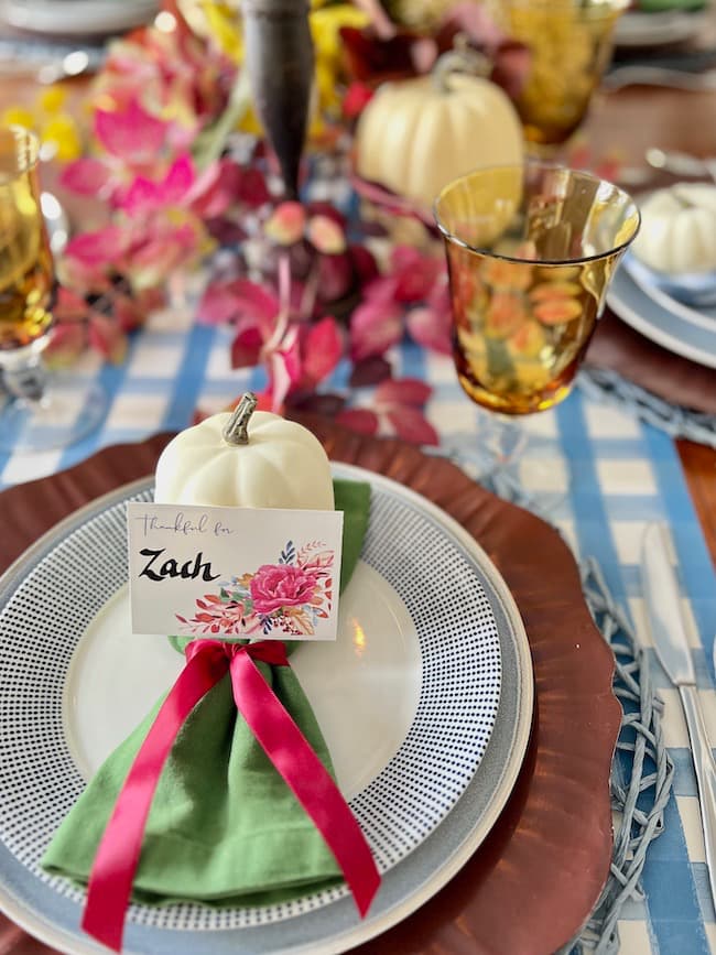 Place settings for Thanksgiving table with printable place cards, green napkin tied with burgundy ribbon, and blue and white plates