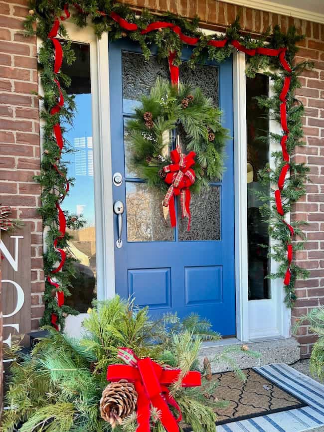 Front porch decorated for Christmas with garland and red velvet ribbon