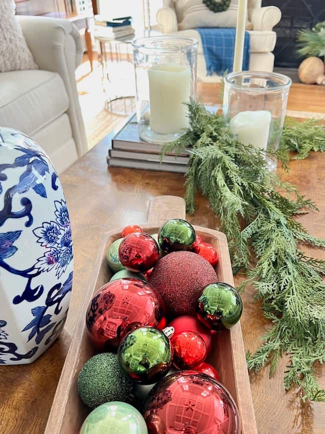 Coffee table decorated for Christmas with garland, candles, Christmas balls in dough bowl and blue and white ginger jar