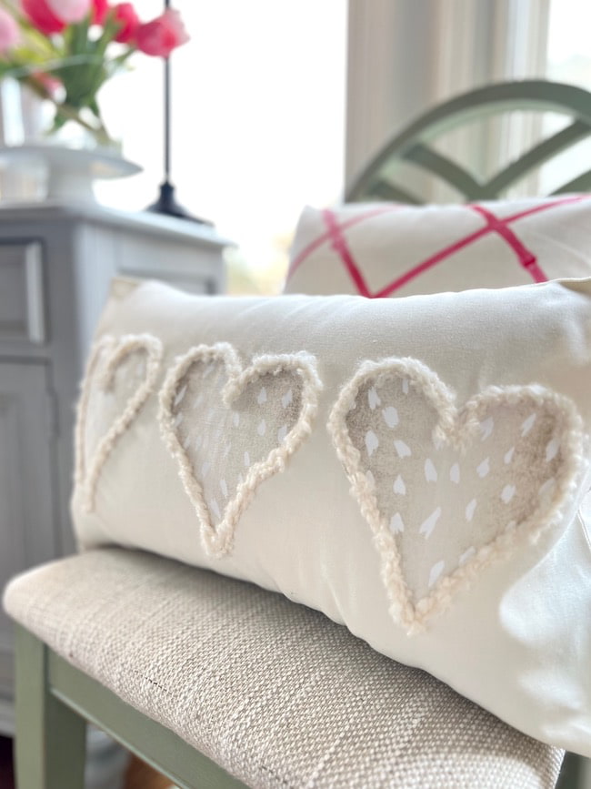Neutral Valentine pillow with three antelope print hearts on a chair with a pink and white hand painted throw pillow
