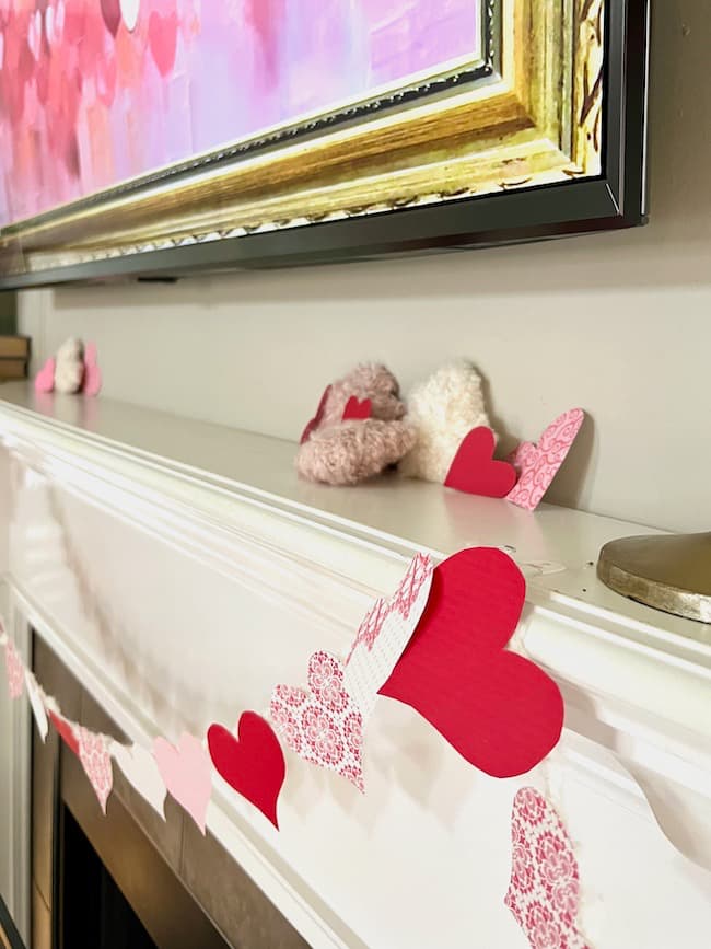 DIY Valentine's Day Garland made with paper hearts from pink and red patterned card stock paper hanging on the mantel.