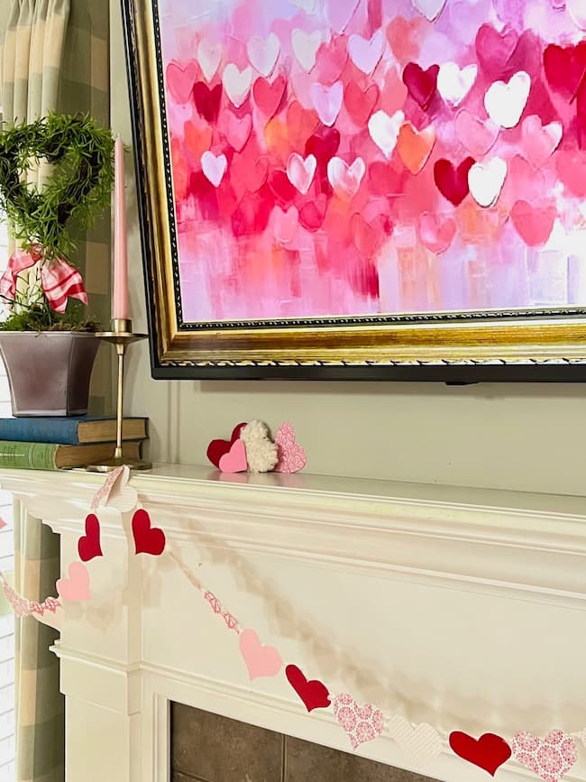 Valentine's Day garland and a heart topiary on mantel with Valentine heart digital art on the tv