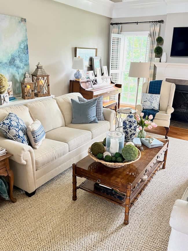 Living room with new Columbia sisal rug from Ballard Designs to replace old jute area rug. Cream sofa with blue patterned accent pillows and Hollywood regency vintage coffee table.