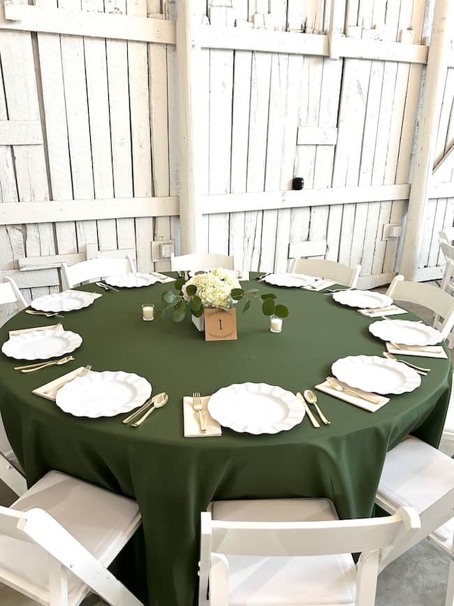 Rehearsal dinner table set with dark green tablecloth and hydrangea centerpieces with white plates at place settings.