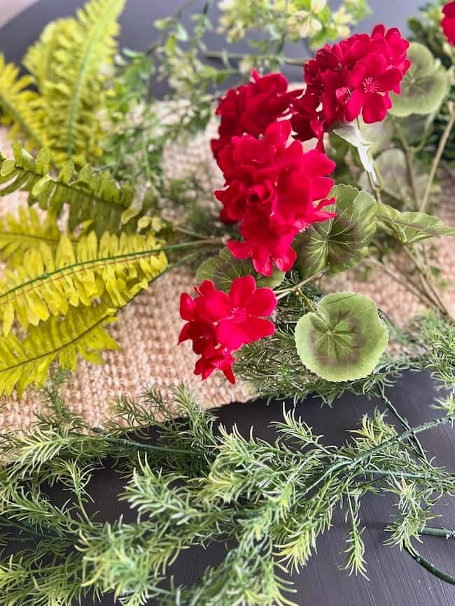 Faux greenery and ferns with faux red geraniums for door hanger