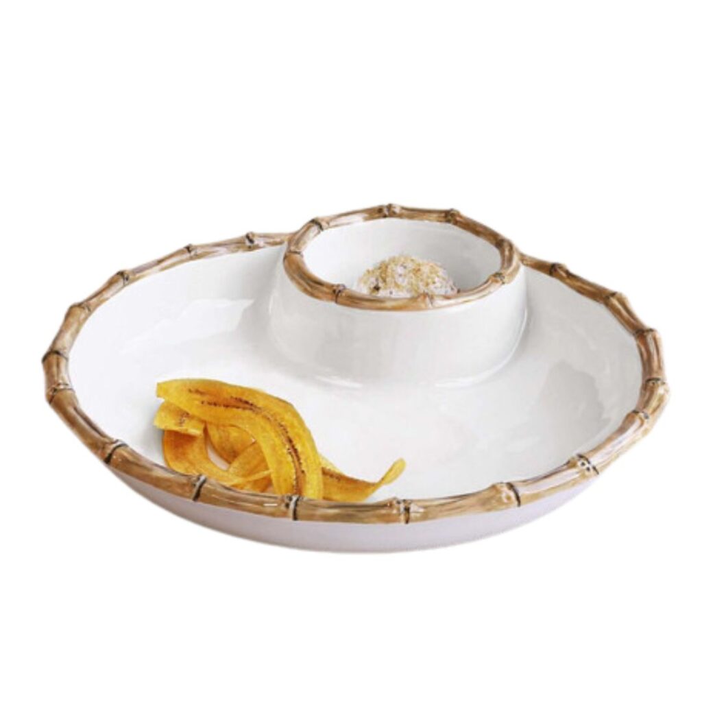 Set a pretty summer table with this round white serving dish featuring a bamboo-style rim and a central dip compartment. The compartment holds a dip, while a few plantain chips are placed on the dish's main surface.