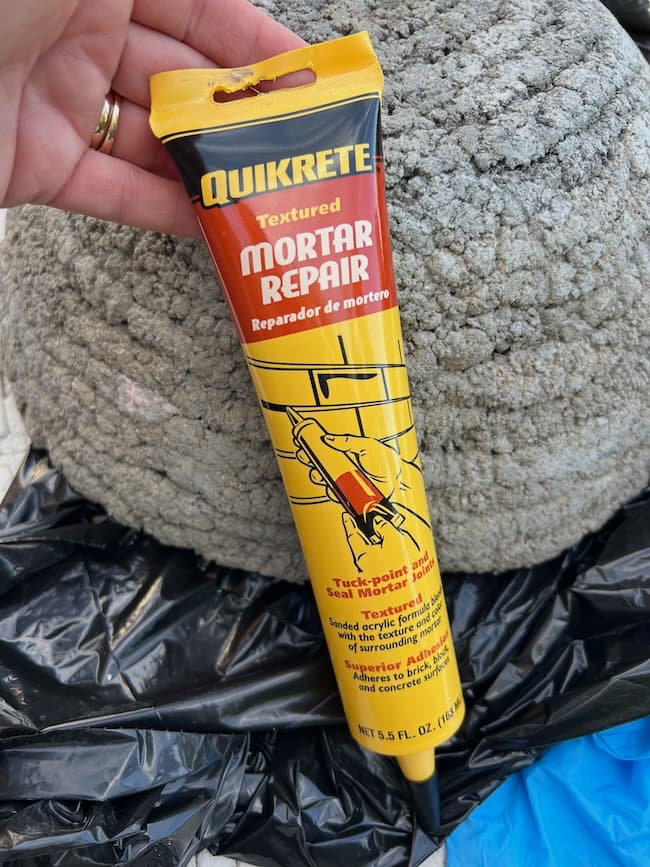 A hand holds a tube of Quikrete Textured Mortar Repair against a textured surface. The yellow tube, with red and black text and illustrations, contains 5.5 fl. oz. (163 ml) of product and includes instructions in English and Spanish—perfect for your next DIY cement planter bowl project.