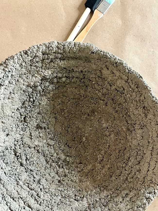 A rustic textured DIY cement planter that is gray in color rests on a counter covered in brown paper waiting to be painted.