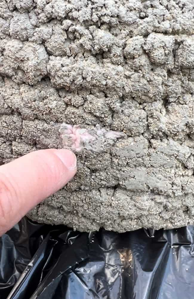 A close-up of a hand pointing at a section of the diy cement planter that in not covered with cement the yarn underneath is poking through into a rough, bark-textured surface.