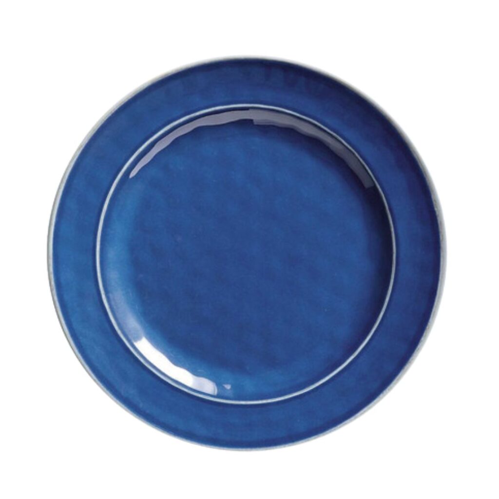 A round, deep blue ceramic plate with a slightly raised rim, featuring a subtle texture and a glossy finish. Set a pretty summer table with this elegant piece, centered against a white background.