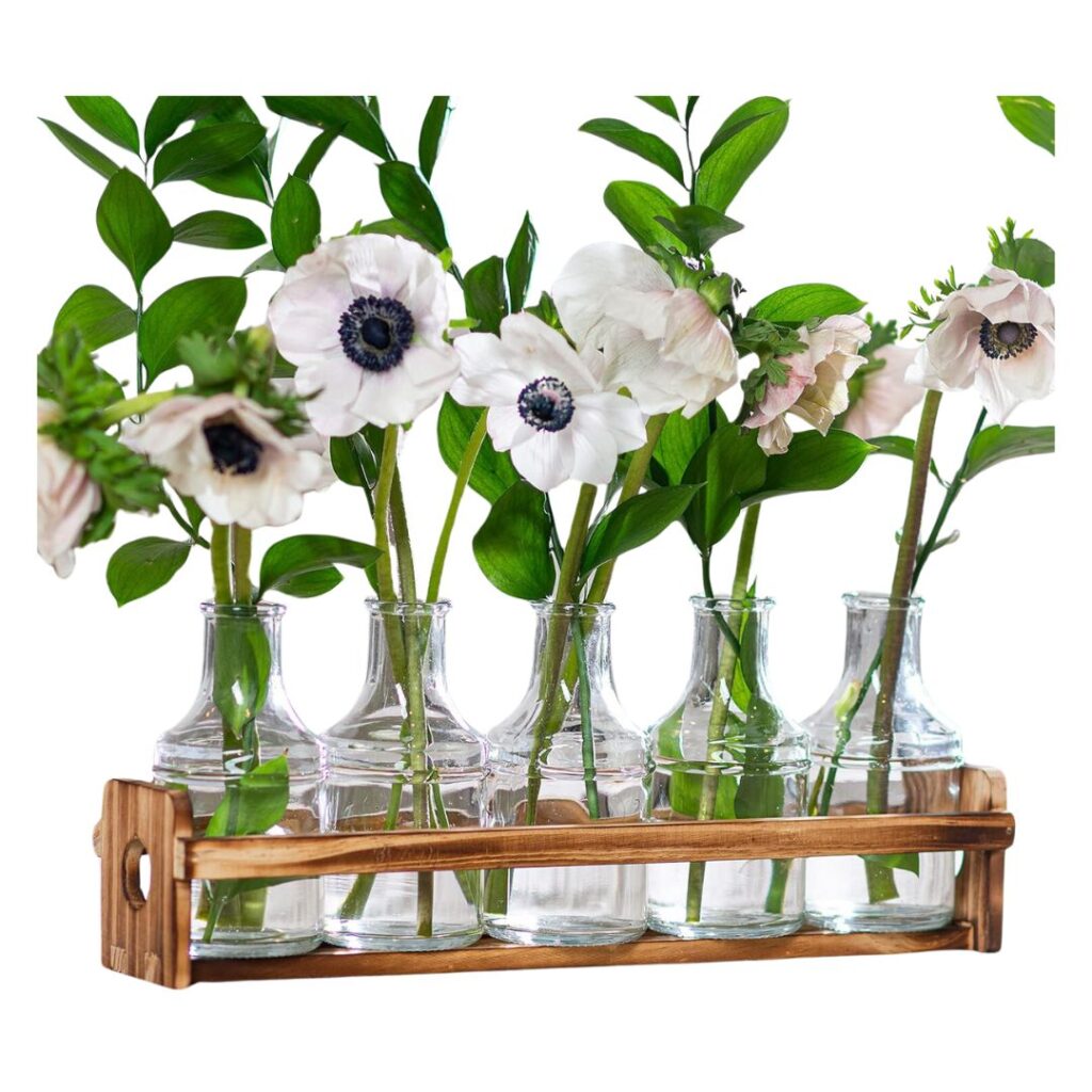 Five glass vases filled with water hold white flowers and green stems, arranged in a wooden holder with two handles for easy carrying. The flowers are evenly spaced, creating a neat and symmetrical display—perfect to set a pretty summer table.