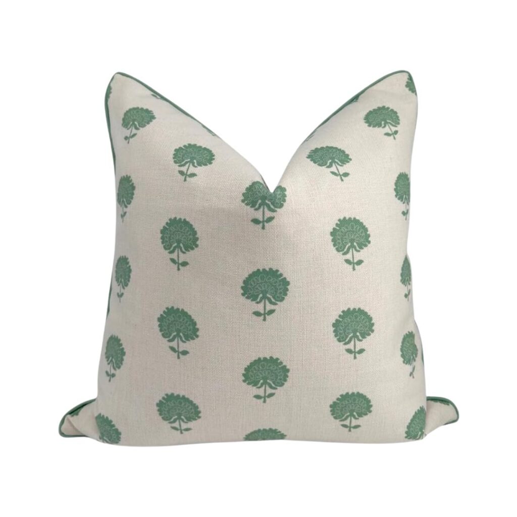 A square throw pillow with cream-colored fabric, adorned with a pattern of green, stylized tree motifs. The edges of the pillow are piped with green fabric that matches the tree pattern. Available on Amazon, this budget-friendly option features a simple yet elegant design perfect for any room.