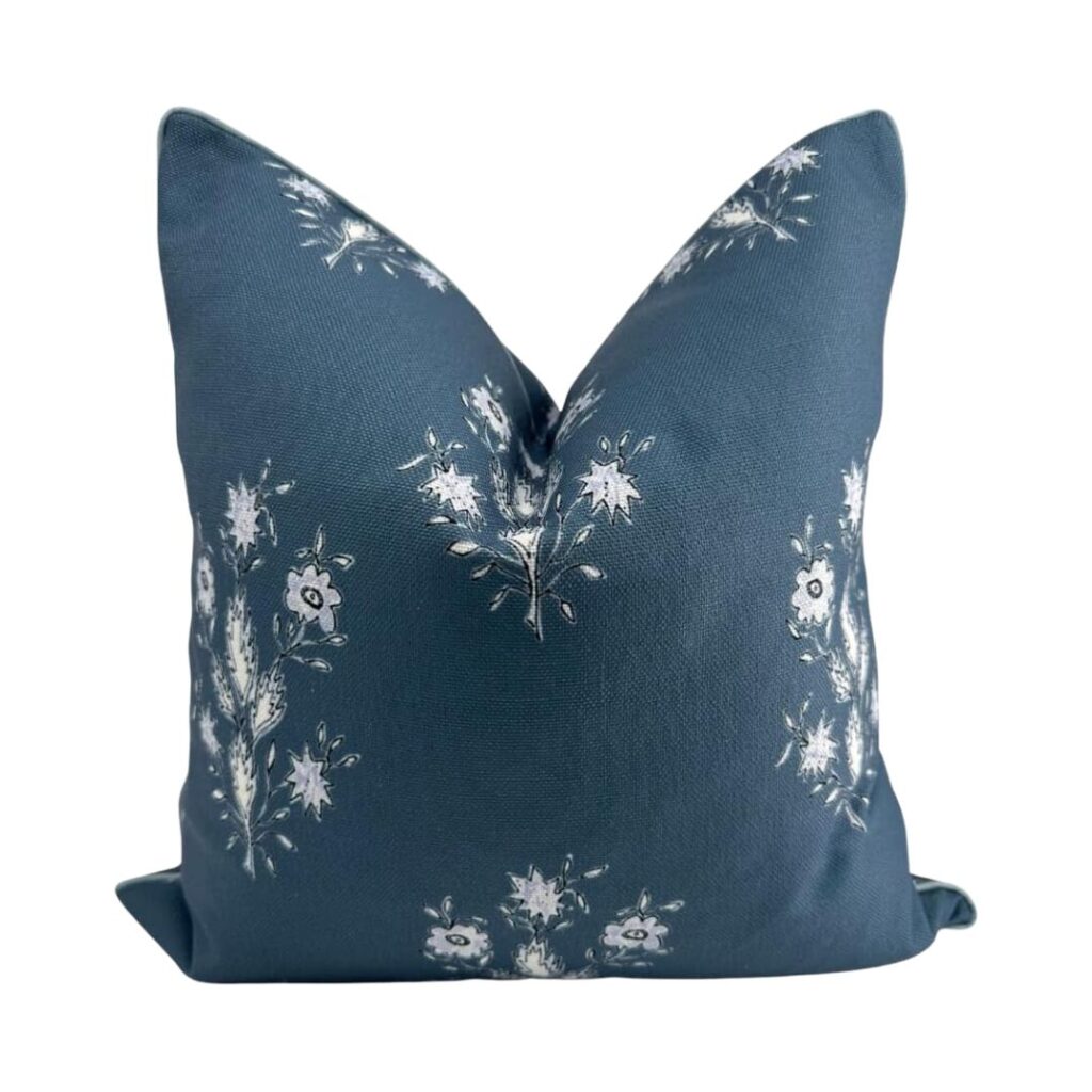 A blue and green throw pillow with a floral pattern featuring white and light blue flowers. The pillow has a smooth texture and is positioned upright against a plain background, offering budget-friendly elegance to any space.