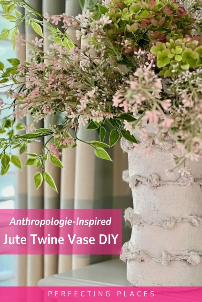 A vase wrapped with jute twine and painted white is filled with lush greenery and light pink and green flowers. The text on the image reads, "Anthropologie-Inspired Jute Twine Vase Tutorial" and "Perfecting Places".