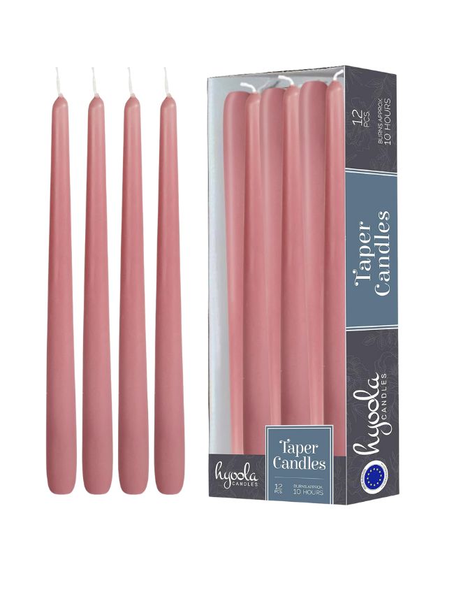 Four pink taper candles stand upright next to a boxed set of twelve identical candles. The box is labeled "Taper Candles" with additional text indicating they are unscented and have a burn time of 10 hours, perfect for end-of-summer decorating ideas with hydrangea-inspired colors.