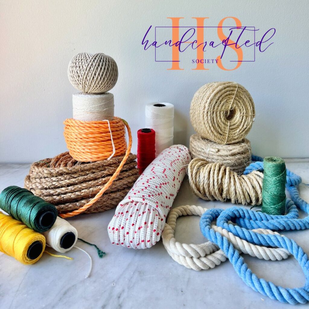 A variety of cords, ropes, and twine in different colors and materials are arranged on a marble surface against a plain white background. A "Handcrafted Society" logo is displayed in the background, reminiscent of an Anthropologie-Inspired tutorial.