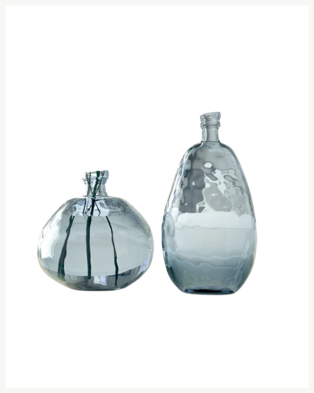 Two glass bottles with irregular shapes and a slight blue tint are displayed against a white background. The bottle on the left, shorter with a wider base, complements cozy living room decor, while the taller, more oval-shaped one warms up your space with its textured surface.