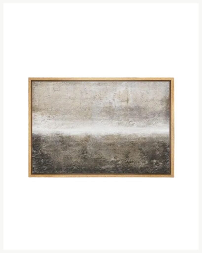 A rectangular, abstract painting with a gradient that transitions from a light, off-white top to a darker, metallic gray bottom, set in a minimalist wooden frame against a white background. Add a moody fall twist to your cozy living room decor and warm up your space with this stunning piece.