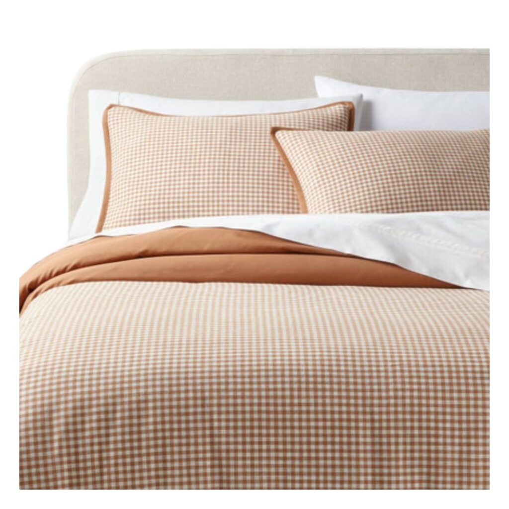 A neatly made bed with a beige upholstered headboard, featuring a light brown and white gingham duvet, two matching gingham pillows, and a white sheet partially covered by a light brown blanket—perfect for incorporating Affordable Target Home Decor into your 2024 Fall Decorating Trends.