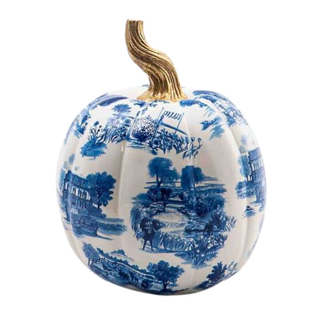 A decorative pumpkin with a white base featuring intricate blue pastoral scenes, reminiscent of toile patterns. The pumpkin has a gold-colored stem and is designed for aesthetic purposes rather than traditional Halloween decor.