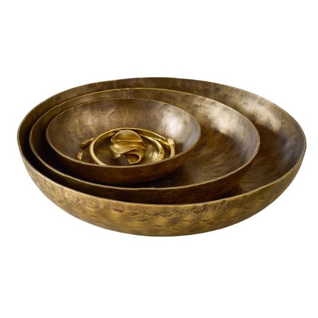 Three nested brass bowls of varying sizes are placed inside each other. The largest bowl holds two smaller bowls, with the smallest one containing what appears to be decorative brass ribbon or loops. The bowls have a textured, hammered finish.