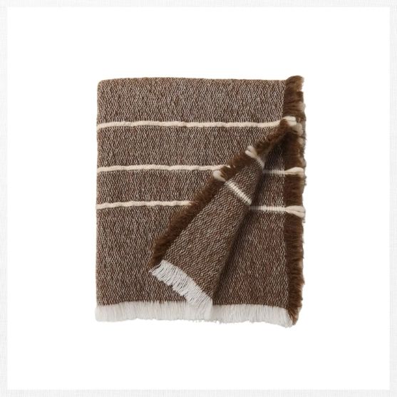 A folded brown woven blanket with white horizontal stripes and white fringes along the edges, displayed on a plain white background—an inviting addition to your fall decor finds.