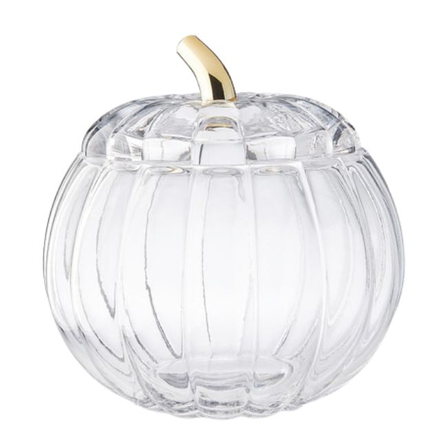 A clear, pumpkin-shaped glass container with a gold-colored stem serving as a lid handle. The container features vertical grooves that resemble the natural texture of a pumpkin.