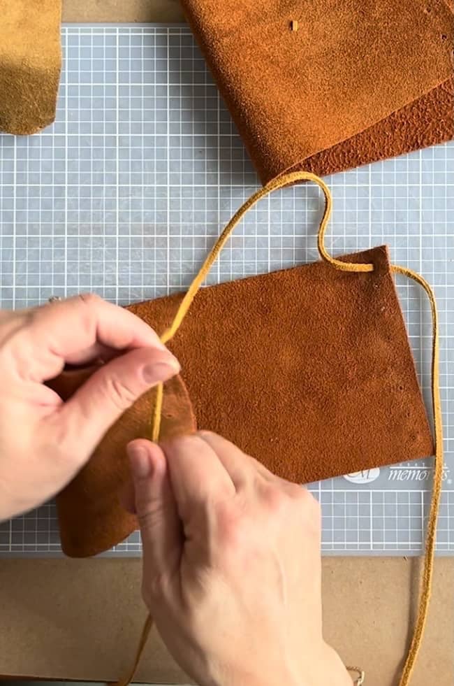 Hands working with brown leather and a yellow leather cord on a crafting mat, creating a leather item.